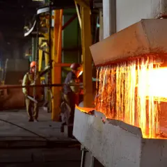 Gorący metal spływa z pieca, iskry sypią się podczas wyżarzania. Pracownicy w hełmach nadzorują proces.