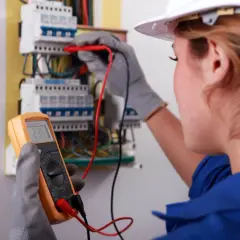 Elektryk w białym kasku wykonuje pomiar instalacji elektrycznej multimetrem.