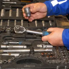 Wybieranie odpowiednich rozmiarów grzechotek z walizki narzędziowej. Ręce mechanika w niebieskim kombinezonie trzymają klucz i nasadkę.