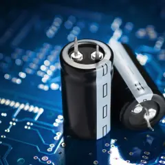 Dwa czarne kondensatory elektrolityczne na niebieskiej płytce drukowanej. Kondensator co to? To kluczowy element elektroniczny.