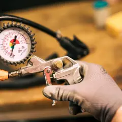 Ręka w rękawicy trzyma pistolet do pompowania z manometrem. Widać skalę ciśnienia i wskaźnik. To narzędzie, które może służyć jako reduktor ciśnienia.