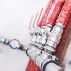 Rząd zaworów z czerwonymi uchwytami, każdy z nich to zawór zwrotny klapowy czy sprężynowy, podłączony do izolowanych rur.