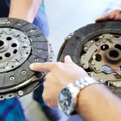 Dwa rodzaje sprzęgieł samochodowych: nowe i zużyte. Mechanik porównuje je, wskazując na różnice w okładzinach.
