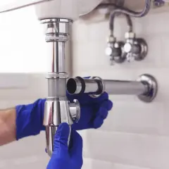 Ręce w niebieskich rękawiczkach montują uszczelkę klinową syfonu.