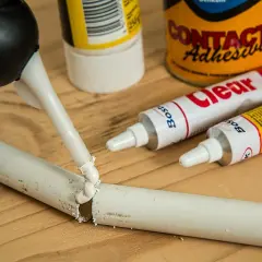 Aplikator z klejem naprawia pękniętą rurkę. W tle tubki kleju "Clear" i "Contact Adhesive" – idealne, by dowiedzieć się, czym skleić plastik.
