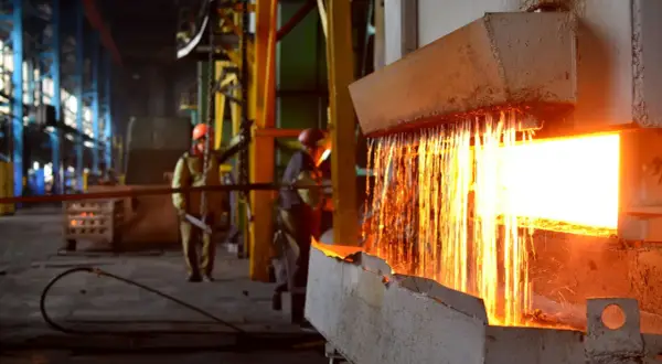 Gorący metal spływa z pieca, iskry sypią się podczas wyżarzania. Pracownicy w hełmach nadzorują proces.