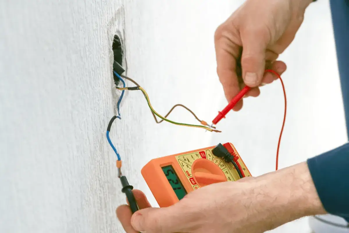 Elektryk sprawdza uziemienie multimetrem. Pomarańczowe urządzenie pokazuje wynik pomiaru.