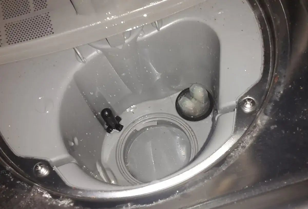 Wnętrze zmywarki Beko z widocznym czarnym elementem i okrągłym otworem z białymi osadami. Może to być przyczyną błędu E01.