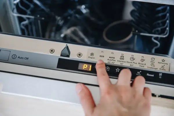 Dłoń naciska przycisk "Reset" na panelu zmywarki Electrolux, co może być pierwszym krokiem, jak zresetować zmywarkę electrolux.