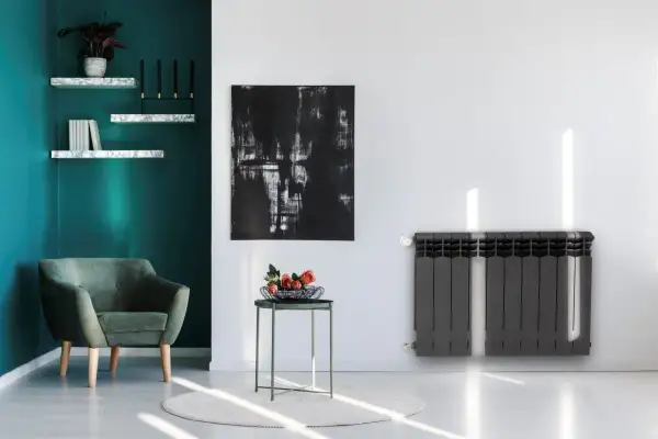 Nowoczesny grzejnik stalowy czy aluminiowy? W stylowym salonie z zieloną kanapą i abstrakcyjnym obrazem, ciemnoszary grzejnik dodaje elegancji.