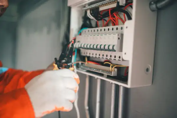 Elektryk w białych rękawiczkach pracuje przy skrzynce z bezpiecznikami. To kluczowy element zabezpieczenia przedlicznikowego.